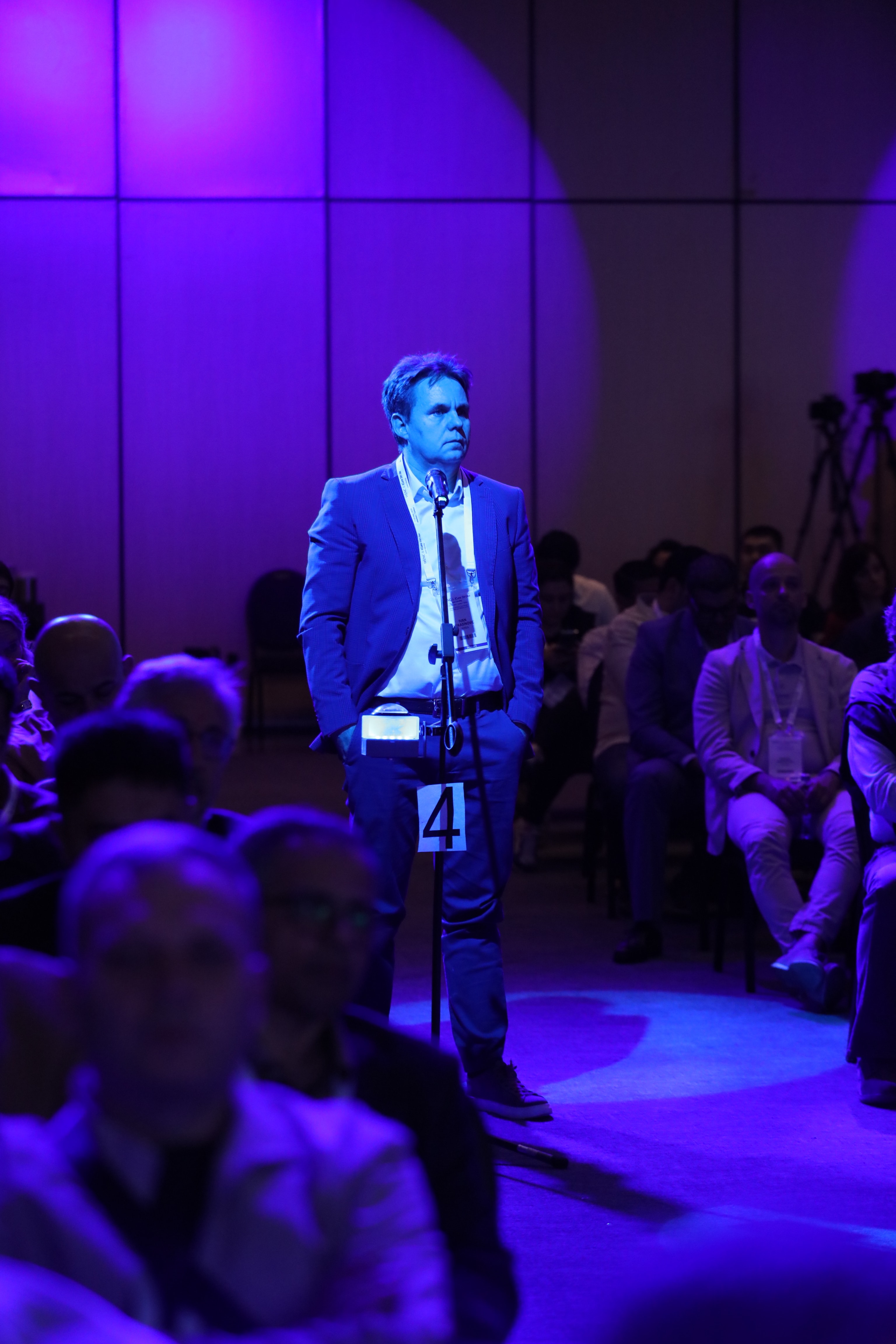Audience member at WLNC 2024 standing at microphone with Spotlight Button in idle mode, ready to engage in live Q&A during an immersive panel session