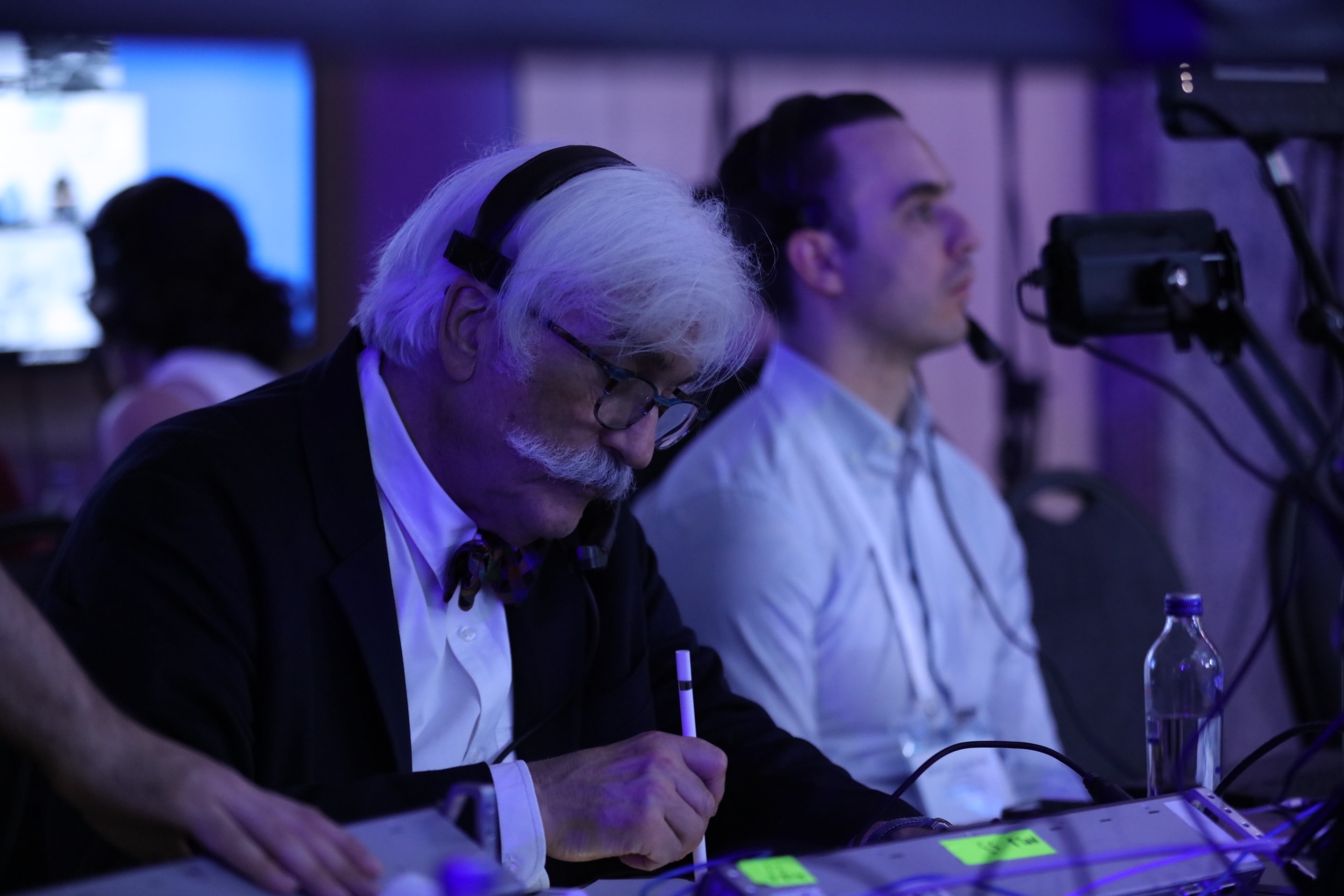 Moderator using a digital pen on the custom-built telestrator interface during WLNC 2024, with AV team coordinating live broadcast in the background